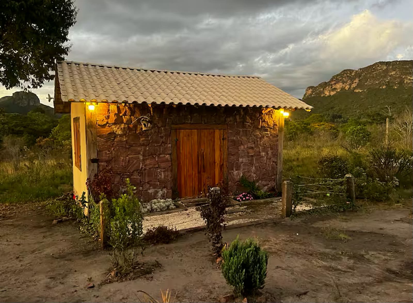 Chalé de pedra da Pousada Portal das Montanhas no entardecer, com as luzes acesas e a serra ao fundo