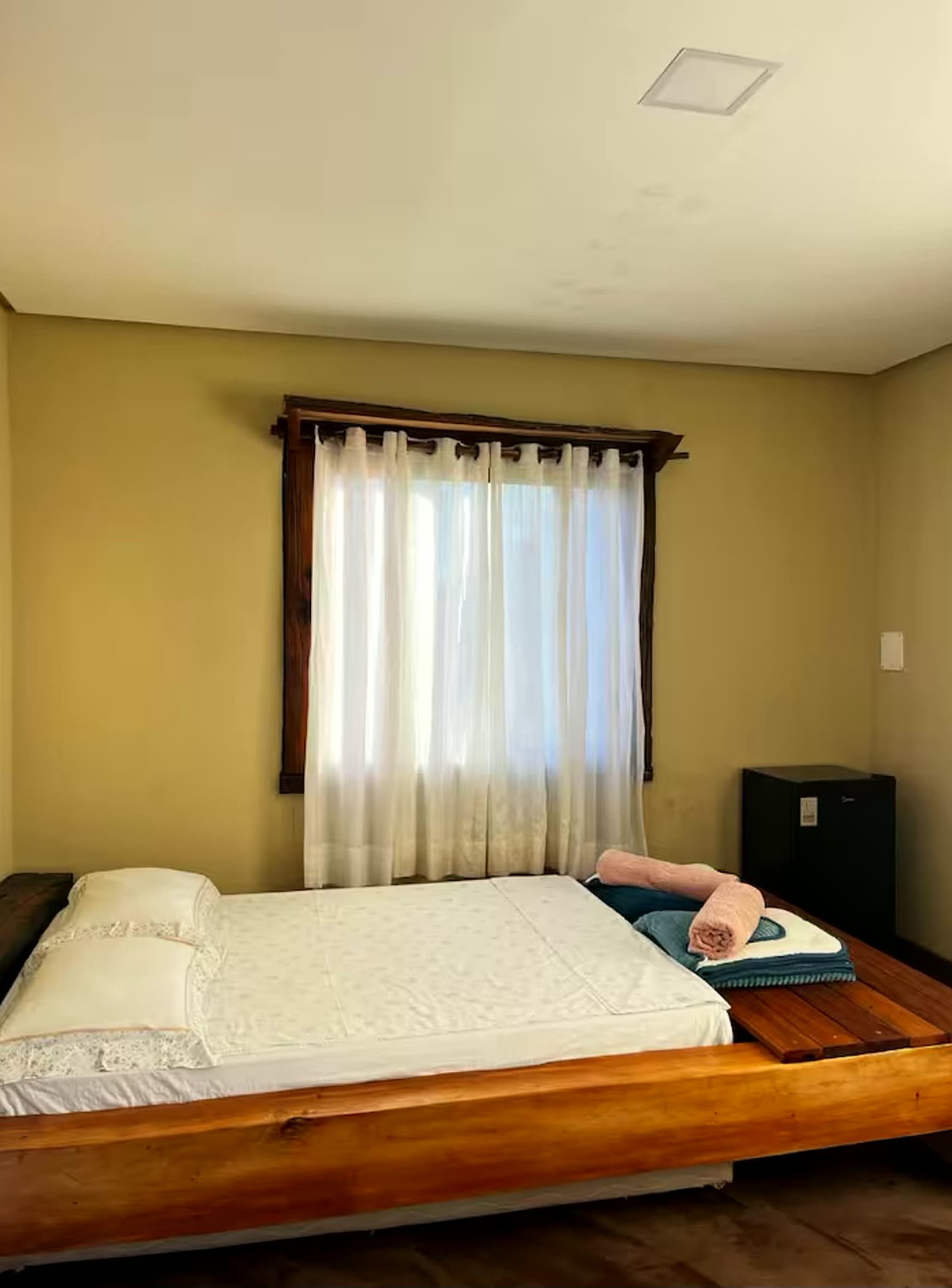 Quarto do chalé 2 com cama de madeira maciça e cortina na janela
