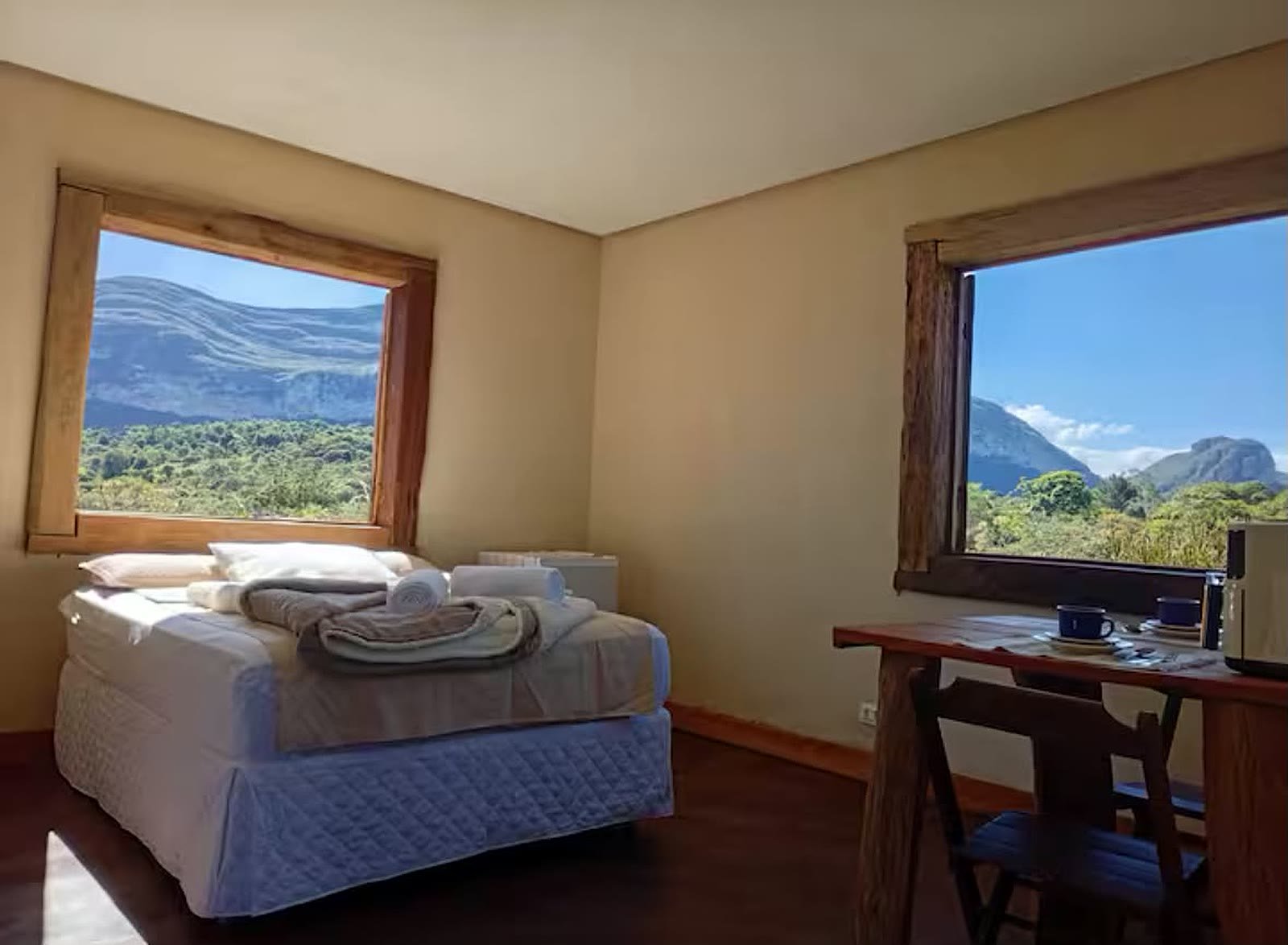 Quarto do chalé 3 com duas janelas abertas mostrando a serra e os morros